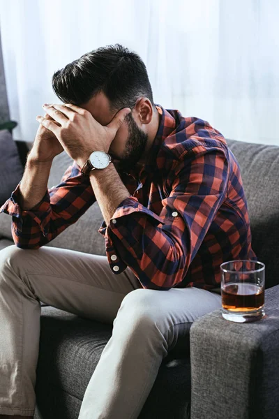 Depressed young man with glass of whiskey sitting on couch — Stock Photo