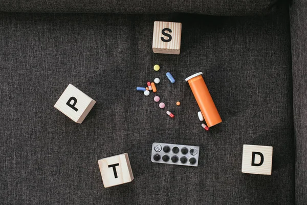 Top view of wooden cubes with posttraumatic stress disorder abbreviation signs (PTSD) lying on couch with various pills — Stock Photo