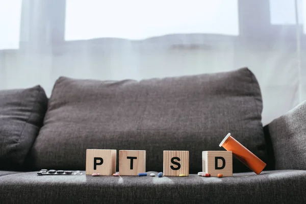 Holzwürfel mit posttraumatischen Belastungsstörungen Abkürzungszeichen (ptsd) liegen mit verschiedenen Pillen auf der Couch — Stockfoto