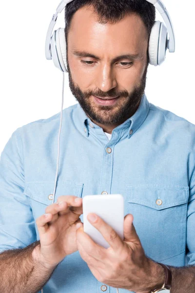 Lächelnder Mann, der mit Kopfhörern Musik hört und das Smartphone isoliert auf weißem Grund benutzt — Stockfoto