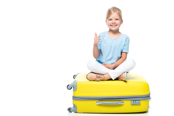 Child sitting on yellow baggage and showing thumb up isolated on white — Stock Photo