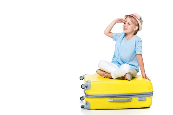 Niño sonriente sentado en el equipaje amarillo aislado en blanco - foto de stock