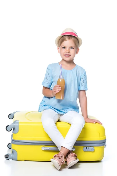 Kid with drink sitting on yellow travel bag isolated on white — Stock Photo