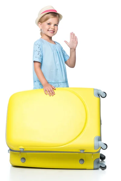 Criança feliz acenando e de pé com saco de viagem amarelo isolado no branco — Fotografia de Stock