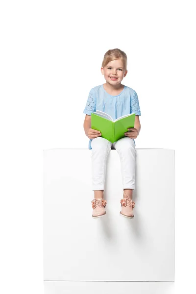 Niño con libro sentado sobre cubo blanco aislado sobre blanco - foto de stock