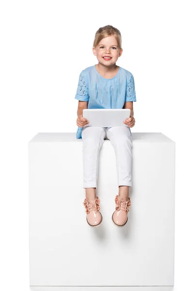 Child using digital tablet and sitting on white cube isolated on white — Stock Photo