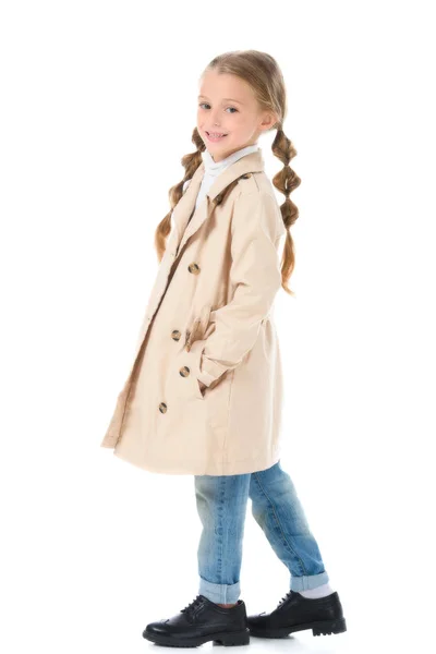 Чарівна дитина позує в бежевому пальто, посміхаючись на камеру, ізольована на білому — стокове фото