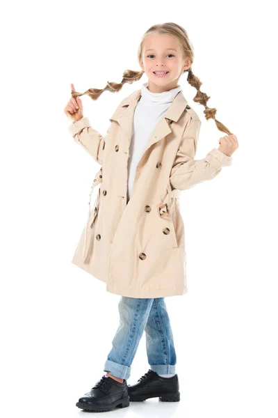 Entzückendes blondes Kind mit Zöpfen posiert in beigem Mantel, isoliert auf weiß — Stockfoto