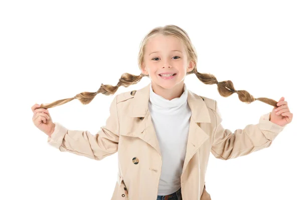 Glückliches Kind mit Zöpfen posiert im beigen Mantel, isoliert auf weiß — Stockfoto