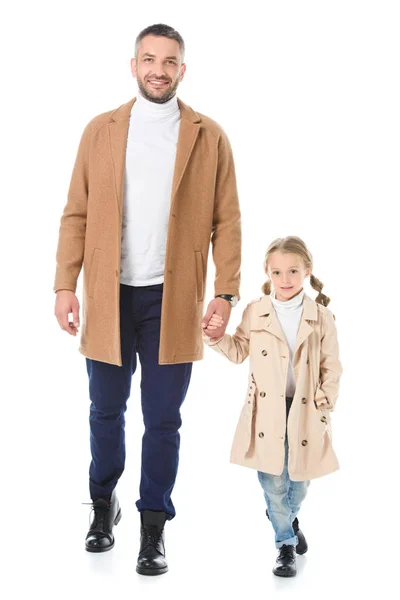 Padre e hija en abrigos beige tomados de la mano y caminando aislados en blanco - foto de stock