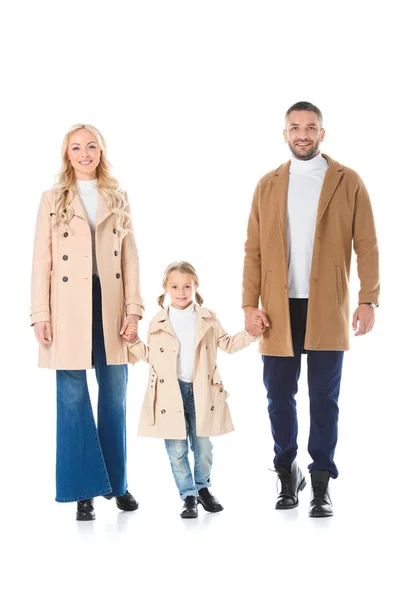 Щасливі батьки тримають руки з чарівною дочкою і позують у бежевих пальто, ізольовані на білому — стокове фото