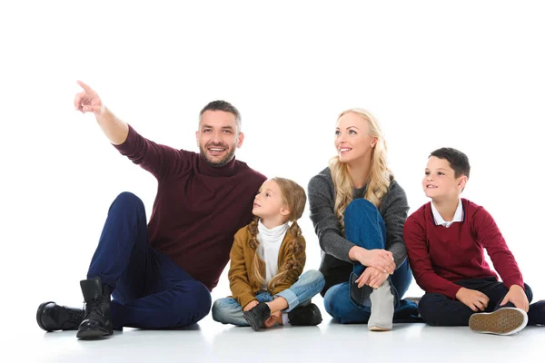 Familia con niños adorables sentados en el suelo, padre mostrando algo aislado en blanco — Stock Photo