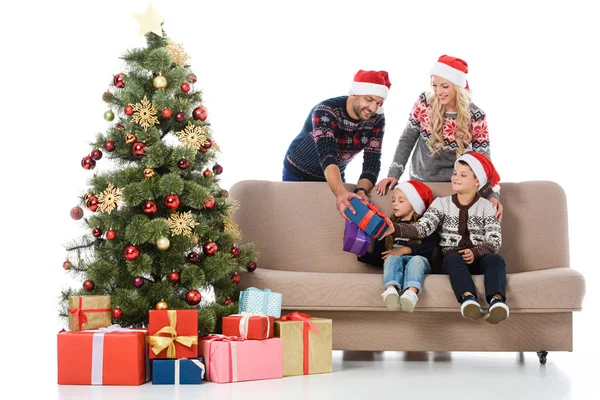 Padres en sombreros de santa dando regalos a los niños sentados cerca del árbol de Navidad, aislados en blanco - foto de stock