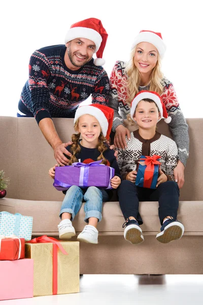 Щаслива сім'я в капелюхах Санти, сидячи на дивані з різдвяними подарунками, ізольовані на білому — стокове фото