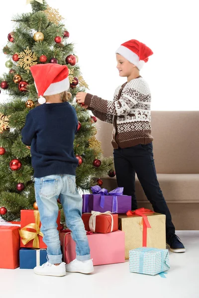 Діти в капелюсі Санти прикрашають різдвяну ялинку подарунковими коробками, ізольовані на білому — стокове фото