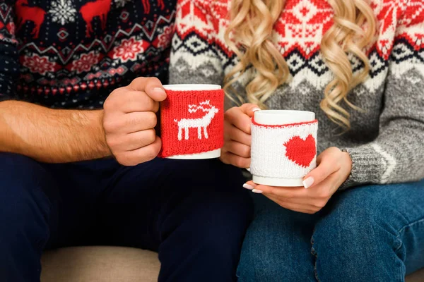 Vista recortada de pareja en suéteres de Navidad sosteniendo tazas con té caliente - foto de stock