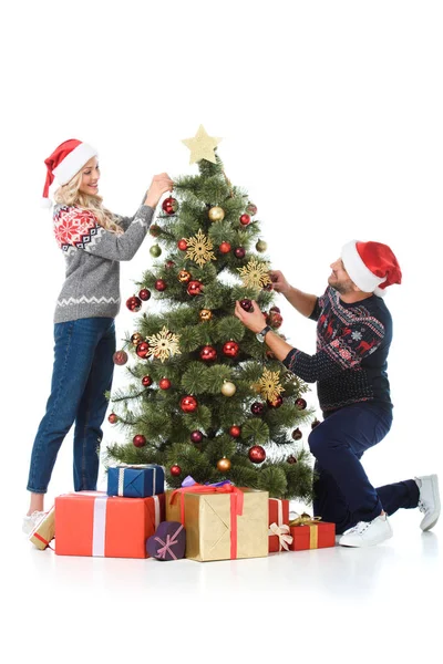 Happy couple in santa hats decorating christmas tree with presents, isolated on white — Stock Photo