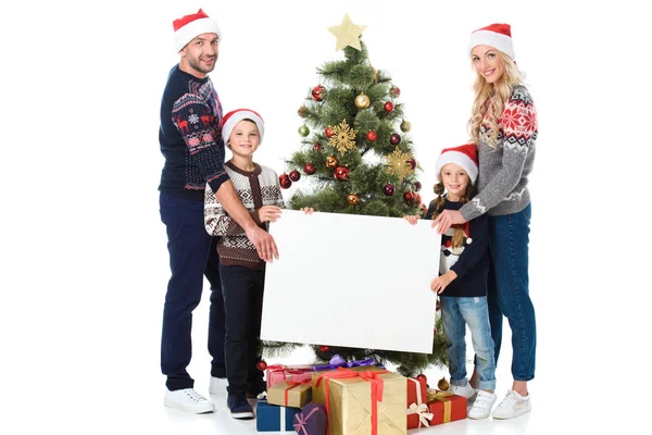 Família feliz segurando placa vazia contra árvore de natal com os pais, isolado no branco — Fotografia de Stock