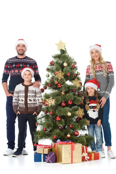 Familia feliz en los sombreros de santa de pie cerca del árbol de Navidad con regalos, aislado en blanco - foto de stock