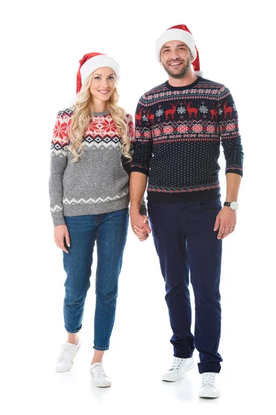 Couple in christmas sweaters and santa hats holding hands, isolated on white — Stock Photo
