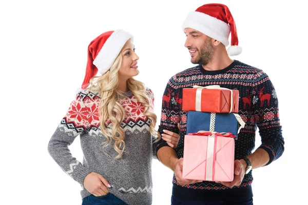 Happy couple in christmas sweaters and santa hats holding presents, isolated on white — Stock Photo