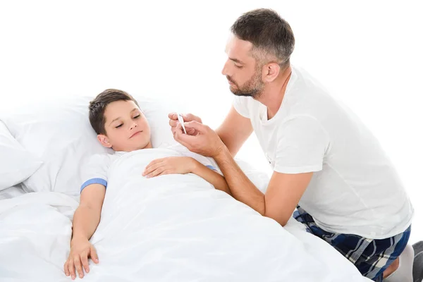 Pai olhando para o termômetro eletrônico, enquanto filho com temperatura deitada na cama, isolado em branco — Fotografia de Stock