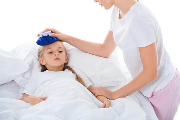 Padre sosteniendo la bolsa de hielo en la cabeza de la hija enferma con la temperatura acostada en la cama, aislado en blanco - foto de stock