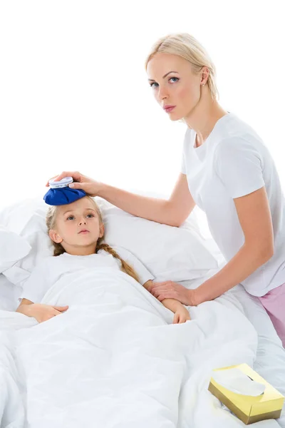 Мати тримає лід на голові хворої дочки з температурою, що лежить у ліжку, ізольована на білому — стокове фото