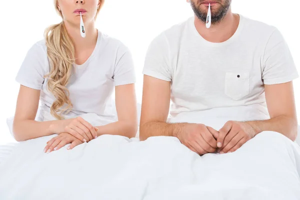 Cropped view of sick couple with electronic thermometers sitting in bed, isolated on white — Stock Photo