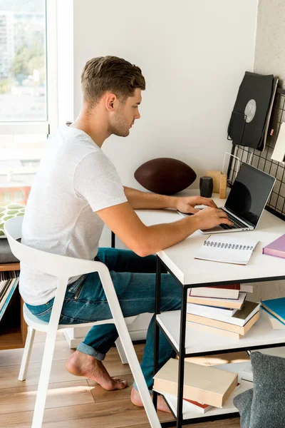 Side view of young man using laptop at table at home office — Stock Photo