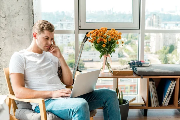 Hombre pensativo en sillón usando el ordenador portátil en casa — Stock Photo