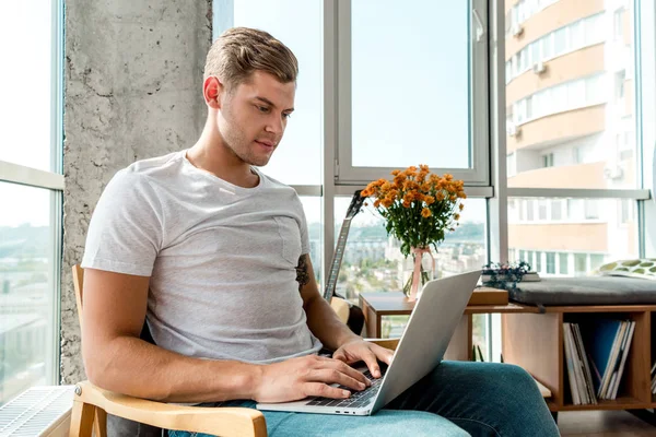 Сфокусированный мужчина в кресле с помощью ноутбука дома — стоковое фото