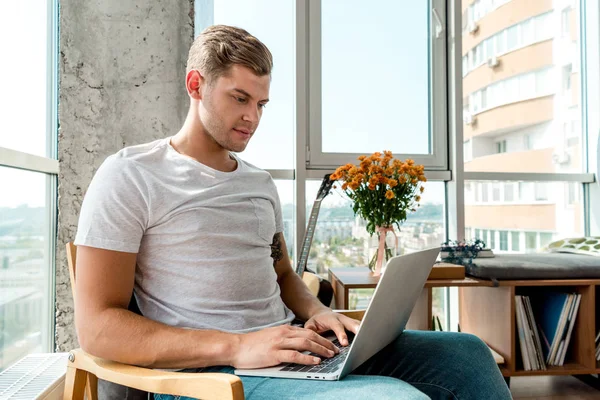 Homme concentré dans le fauteuil en utilisant un ordinateur portable à la maison — Photo de stock