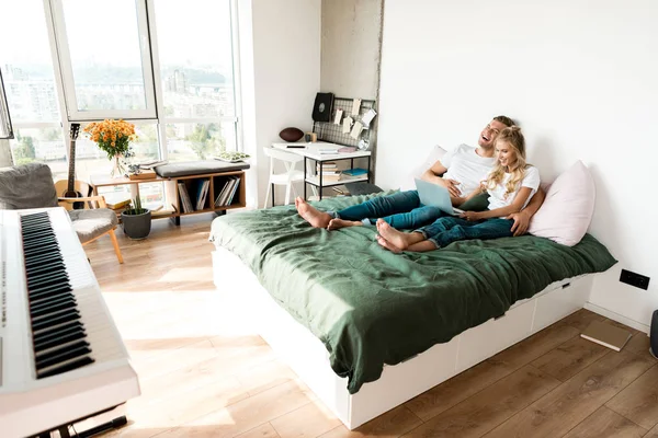 Щаслива пара з цифровим ноутбуком відпочиває на ліжку вдома — стокове фото
