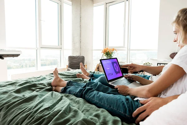 Vista parcial de la pareja usando portátil digital con letras de compras web en la pantalla mientras descansa en la cama en casa - foto de stock