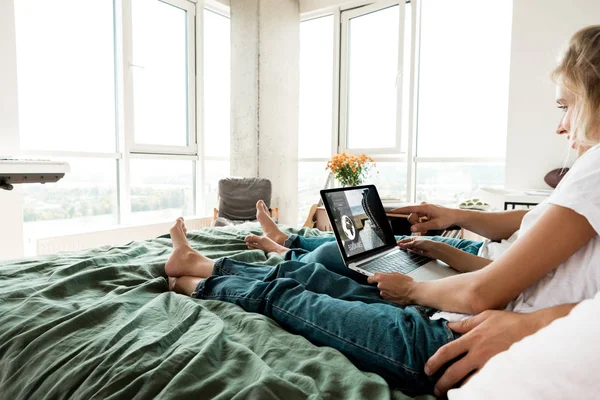 Partial view of couple with digital laptop with booking lettering on screen resting on bed at home — Stock Photo
