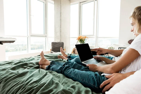 Vue partielle du couple avec ordinateur portable numérique avec écran vierge reposant sur le lit à la maison — Photo de stock