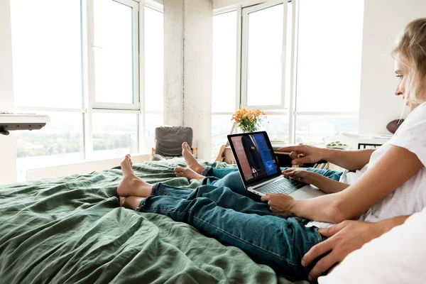 Vue partielle du couple à l'aide d'un ordinateur portable numérique avec panneau de réservation à l'écran tout en se reposant sur le lit à la maison — Photo de stock