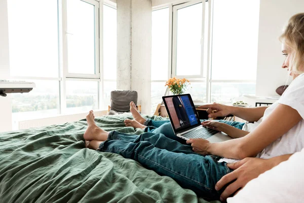 Vista parcial de la pareja usando portátil digital con signo de reserva en la pantalla mientras descansa en la cama en casa - foto de stock