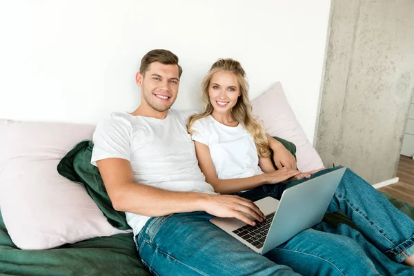 Sorridente giovane coppia con computer portatile digitale a riposo sul letto a casa — Foto stock