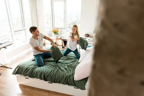 Young couple in love having pillow fight on bed at home — Stock Photo