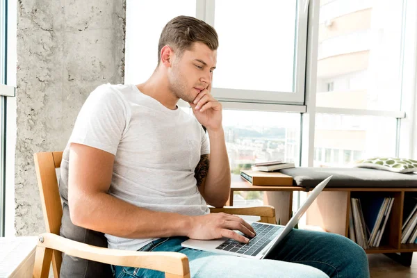 Hombre pensativo en sillón usando el ordenador portátil en casa - foto de stock