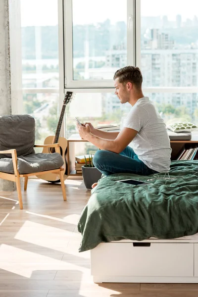 Seitenansicht eines Mannes, der sein Smartphone benutzt, während er zu Hause im Bett liegt — Stockfoto