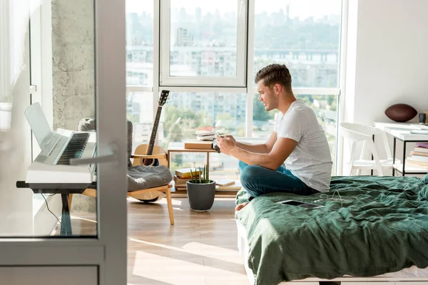Seitenansicht eines Mannes, der sein Smartphone benutzt, während er zu Hause im Bett liegt — Stockfoto