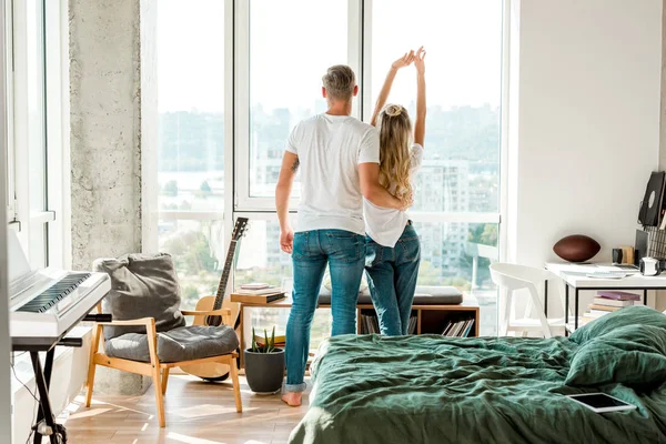 Vue arrière du jeune couple debout à la fenêtre — Photo de stock