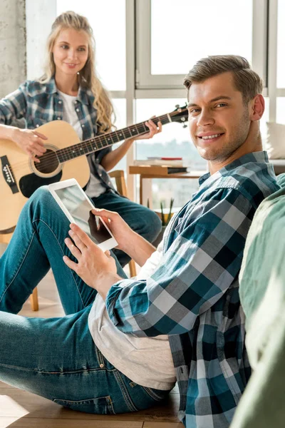 Smiling man with digital tablet and girlfriend with acoustic guitar at home — Stock Photo