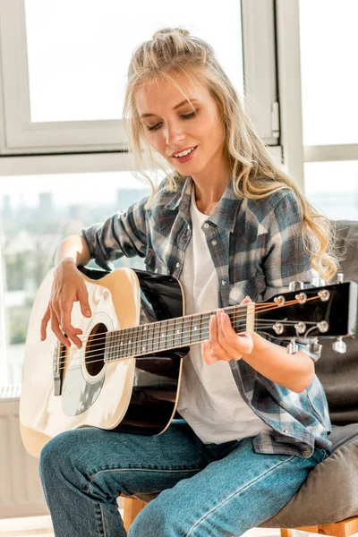 Jeune belle femme en vêtements décontractés jouant de la guitare acoustique à la maison — Photo de stock