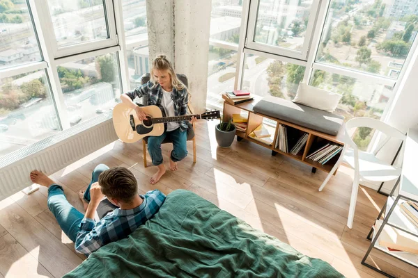 Visão de alto ângulo do homem usando tablet digital enquanto namorada tocando guitarra acústica em casa — Fotografia de Stock
