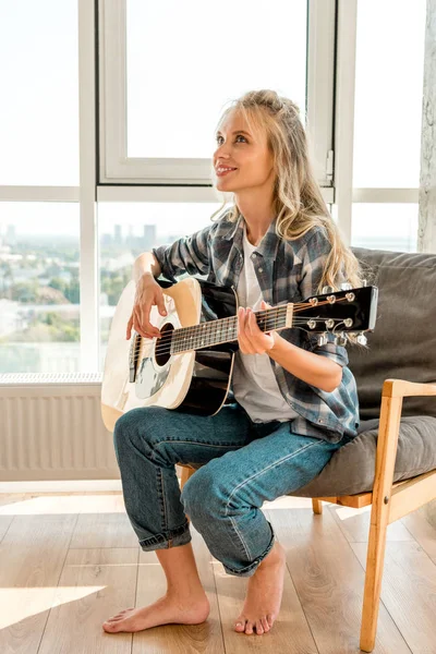 Молода красива жінка-гітаристка в повсякденному одязі грає на акустичній гітарі вдома — стокове фото