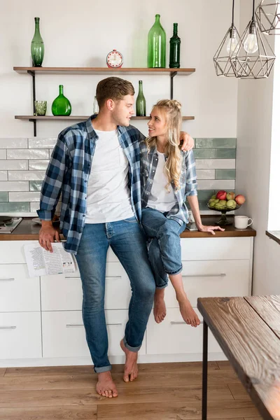 Sonriente pareja amorosa en ropa casual en la cocina en casa - foto de stock